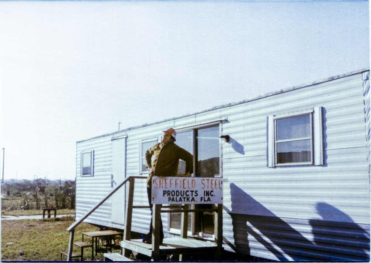 Image 015. James MacLaren, site representative for Sheffield Steel, who furnished the structural steel for the Rotating Service Structure at Space Shuttle Launch Complex 39-B, Kennedy Space Center, Florida, stands atop the entryway stair to the Sheffield Steel field trailer and strikes himself a pose for the camera, during a lighter moment at work. Photo by Eugene Hajdaj.